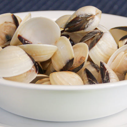 Primer plano de almejas cocidas en un bol blanco, resaltando la textura y los tonos naturales del marisco, ideal para representar platos de almejas en gastronomía.