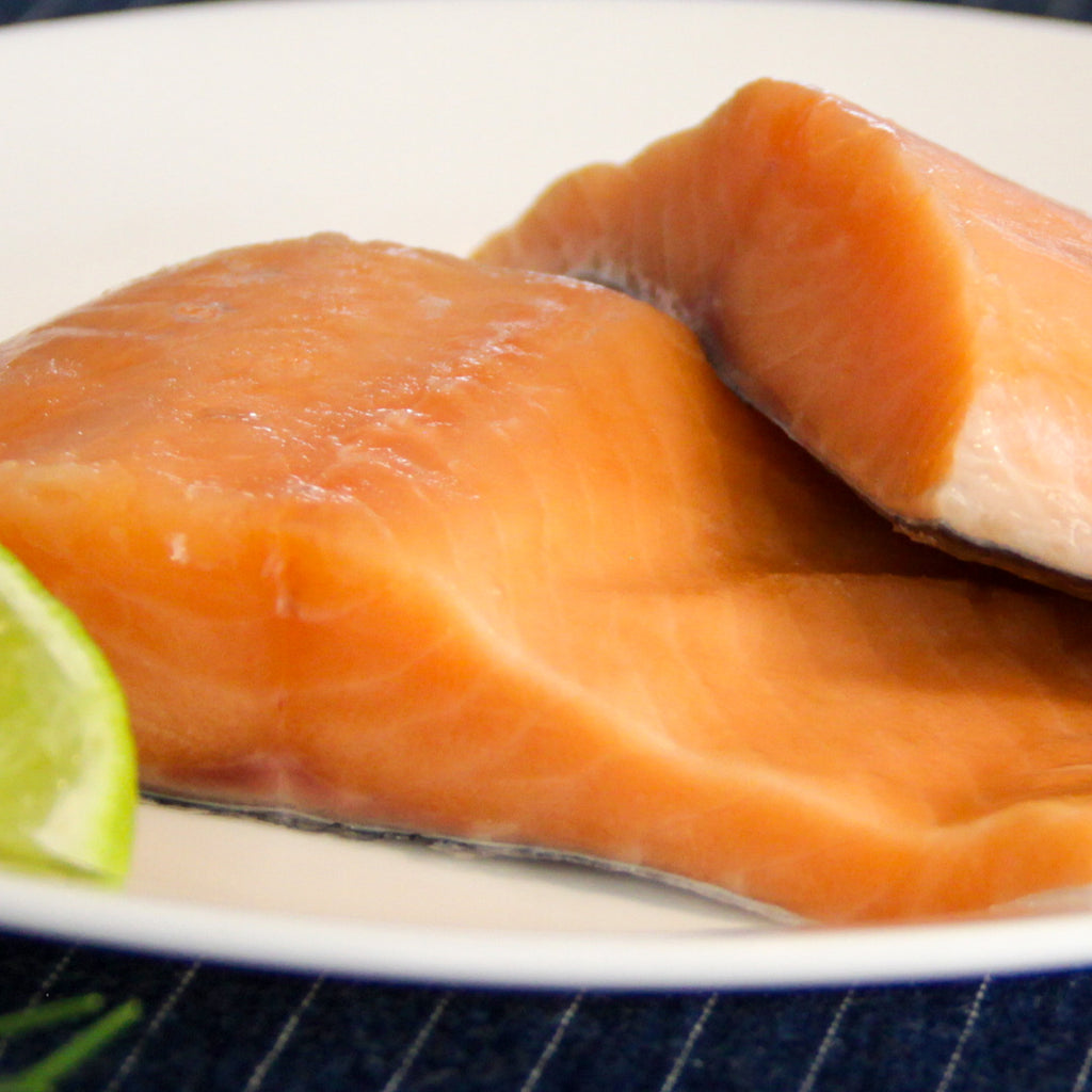 Un primer plano de trozos de salmón fresco sobre un plato blanco, con detalle de la textura suave del pescado y una guarnición de lima, ideal para resaltar recetas con salmón en blogs de cocina o menús de restaurantes.