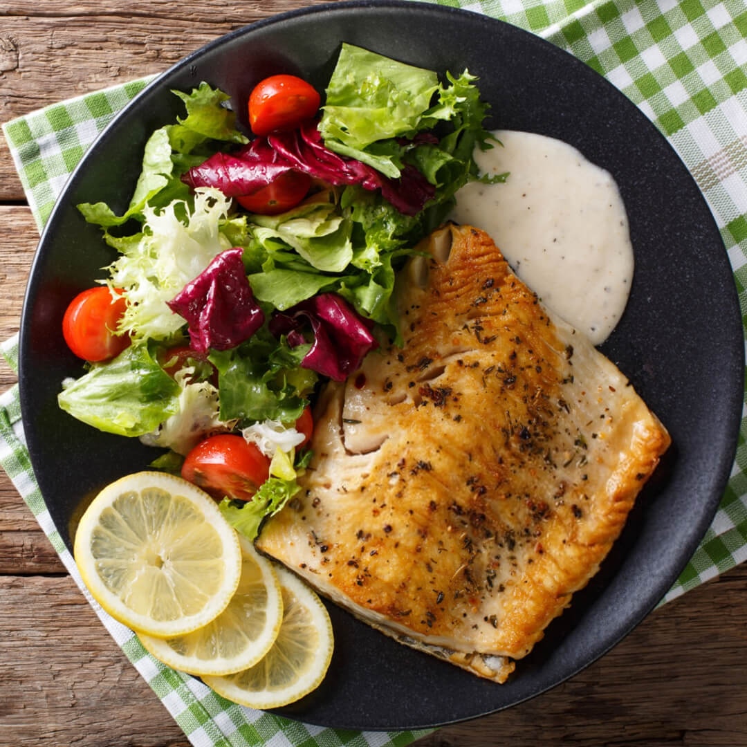 Un plato de filete de marlin blanco a la plancha acompañado de una ensalada y aderezo.