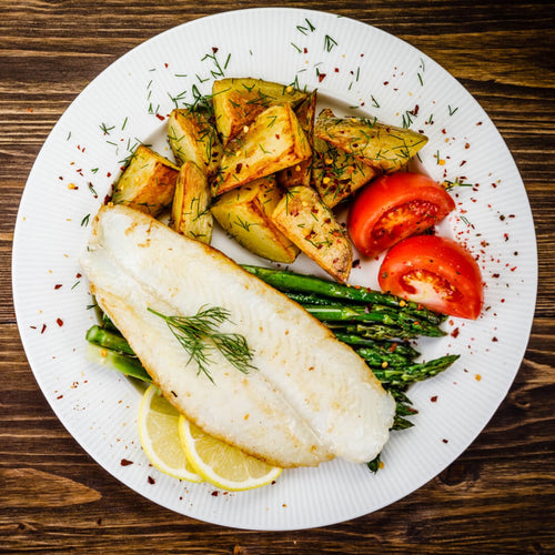 Un filete de corvina al vapor acompañado de espárragos, papas y tomate