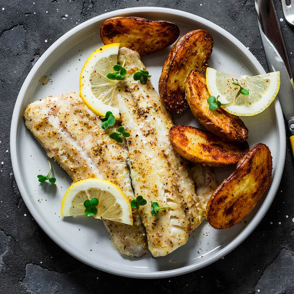 Dos filetes de congrio al horno acompanado de papas wedges decorado con limón en medias lunes y microgreens