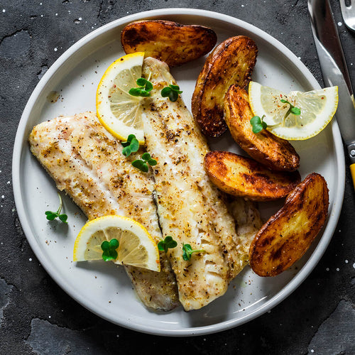 Dos filetes de congrio al horno acompanado de papas wedges decorado con limón en medias lunes y microgreens